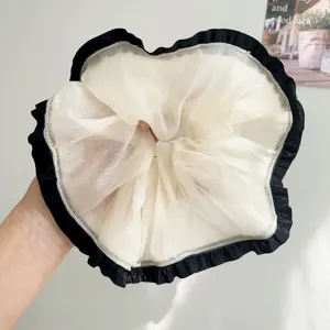 Gedetailleerd beeld van een crème mesh scrunchie met zwarte ruches voor het haar