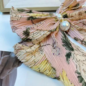 Détail d'une pince à cheveux nœud en mousseline fleurie rose avec des perles élégantes