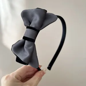 Dettaglio di un cerchietto elegante con fiocco in raso grigio e velluto nero da donna.