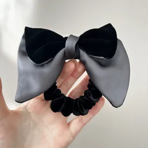 Dettaglio di un elegante elastico per capelli con fiocco in velluto nero e raso grigio.