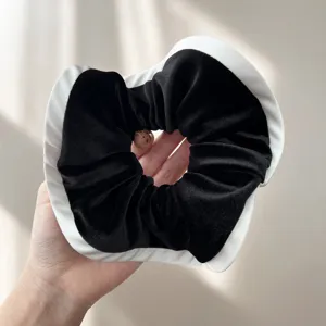 Dettaglio di un elastico per capelli in velluto nero con bordo bianco a contrasto in mano