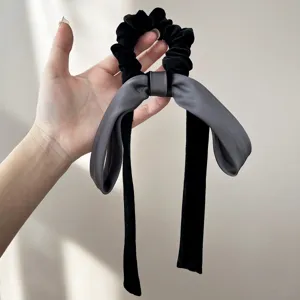 Dettaglio di un elastico per capelli in velluto con fiocco e lunghi nastri grigi e neri.