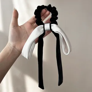 Dettaglio di un elastico in velluto nero con un grande fiocco bianco e lunghi nastri
