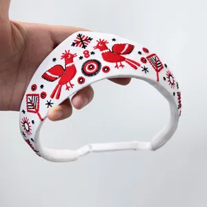 Detailansicht eines weißen Vintage-Stirnbands mit roter Sonnenvogel-Volksstickerei