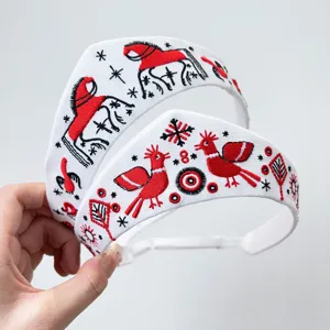 Detailansicht eines weißen Stirnbandes mit roter und schwarzer Sonnenvogel-Stickerei.