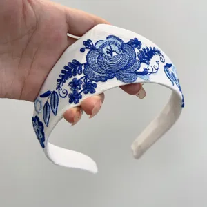 Detailansicht der aufwendigen blauen Sonnenvogel- und Blumenstickerei auf weißem Haarband