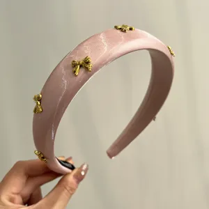 Close-up of pink satin padded headband featuring gold metal bow embellishments