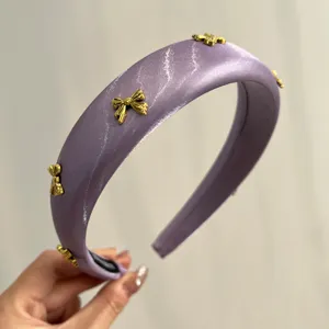 Detailed view of a purple satin padded headband featuring elegant gold bow charm accents.
