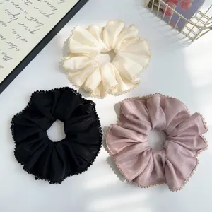 Three elegant satin scrunchies with crystal beaded edges in cream, black, and pink.