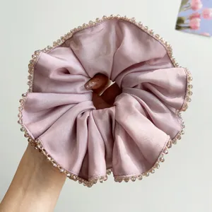 Close-up detail of a pink satin scrunchie featuring elegant crystal bead edging.