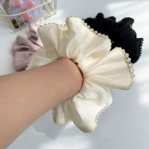 Elegant cream satin scrunchie with crystal beaded edges worn on wrist close-up detail