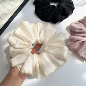Close-up of a satin scrunchie with delicate crystal beaded edges in cream color