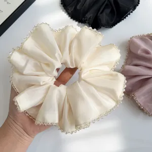 Detail view of a cream satin scrunchie with crystal beaded edges held by hand