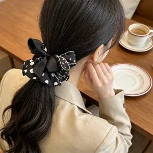 Elegant lifestyle view of a black polka-dot bow scrunchie worn on a low ponytail