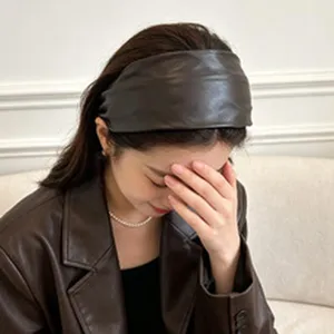 Close-up detail showing a stylish brown faux leather wide headband on a model's head.