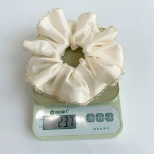 Elegant cream satin scrunchie with crystal beads weighed on a green digital scale