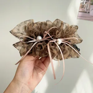 Gros plan d'une pince banane en tulle léopard avec des rubans roses et des perles.