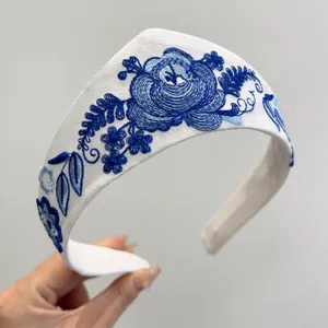 Detailansicht eines weißen Vintage-Haarbands mit eleganter blauer Stickerei.