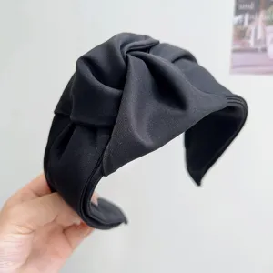 Primer plano de una diadema ancha de tela negra con diseño de nudo y textura suave.