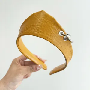 Dettaglio di un cerchietto vintage in ecopelle gialla testurizzata con anelli di metallo