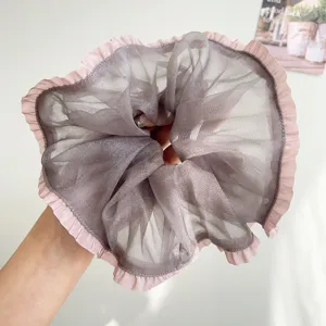 Detailopname van een grote grijze mesh scrunchie met elegante roze geplooide randen