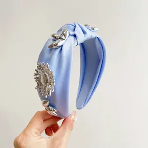 Close-up of blue satin knotted headband with metallic silver flowers and petal details.
