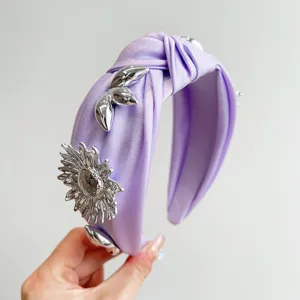 Close-up detail of metallic silver flower charm on purple knotted wide headband.