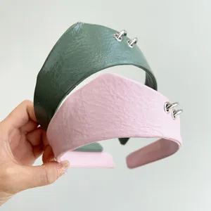 Dettaglio ravvicinato di cerchietti in pelle testurizzata verde e rosa con anelli in metallo.