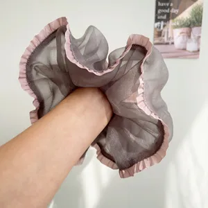 Detailweergave van een grijze mesh scrunchie met roze ruches gedragen om de pols