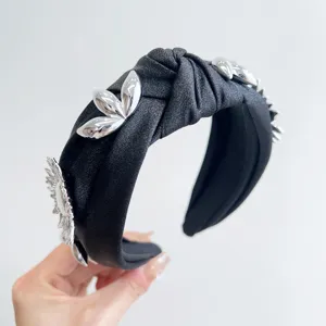 Detailed view of a black knotted wide headband decorated with silver metallic flowers