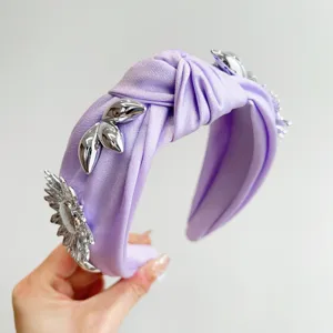Detail showing the silver metal flower and leaf accents on the purple knotted headband.