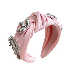 Pink knotted wide headband with silver metallic flower accents for high-volume hair style.