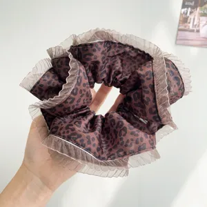 Close-up detail of a large leopard print hair scrunchie with elegant pleated lace edges