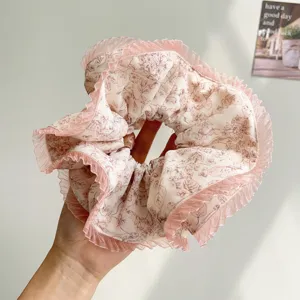 Detailed view of a soft floral print scrunchie with pink pleated edges held in hand