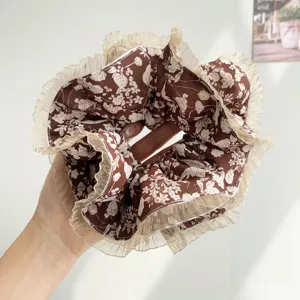 Close-up of a brown floral scrunchie featuring elegant cream pleated mesh trim edges