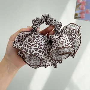 Macro detail of a large leopard print ruffled hair scrunchie with brown edging held in hand