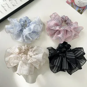 A detailed macro view of four colorful ruffled plaid scrunchies on a white table