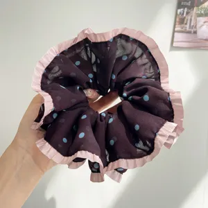 Détail d'un chouchou en résille à pois violets avec des bords à volants roses en main.