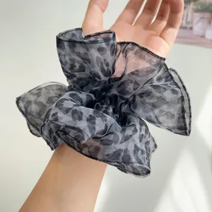 Détail d'un chouchou volumineux en maille transparente léopard porté au poignet.