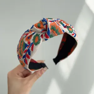 Primer plano de una diadema bohemia anudada con bordados florales étnicos coloridos.