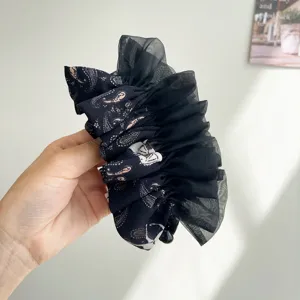 Détail de la pince à cheveux en organza noir à volants et tissu à motifs cachemire