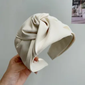 Detalle de una elegante diadema de tela color crema con diseño de nudo superior.