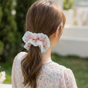 Close-up of a floral pleated mesh scrunchie styled on a woman's hair in a garden
