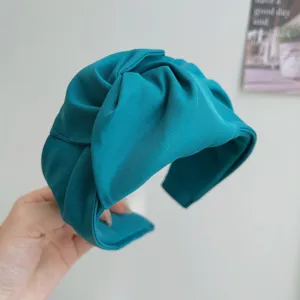 Detalle de una diadema de tela azul turquesa con diseño de nudo y textura de canalé.