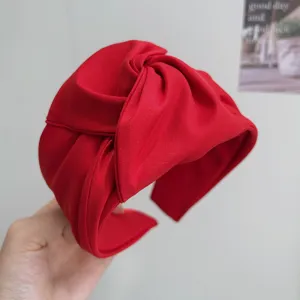 Primer plano de una diadema ancha anudada de tela roja vibrante con detalles.