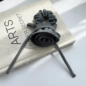 Nahaufnahme eines grauen plissierten Rosen-Haargummis mit eleganten langen Bändern auf Buch