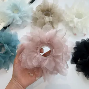 Vista dettagliata di una mano che tiene un grande scrunchie a fiore in organza rosa con perle