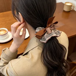 Detailed close-up of a brown plaid bow scrunchie styled on a woman's wavy ponytail