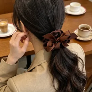 Detailed view of a model wearing a brown ribbon bow scrunchie on a ponytail in a cafe