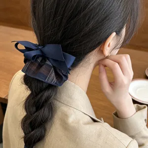 Detailed view of an elegant navy blue plaid bow scrunchie on a braided ponytail hairstyle